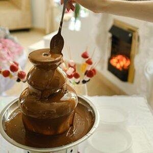 Two-tier chocolate fountains displayed at an event with treats.