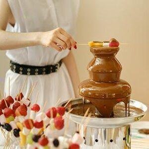 Chocolate fountain with strawberries on skewers being dipped.
