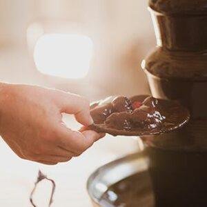 Hand holding plate while scooping chocolate from a fountain.