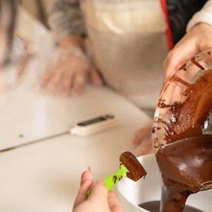 Person dipping fruit into a chocolate fountain at an event.