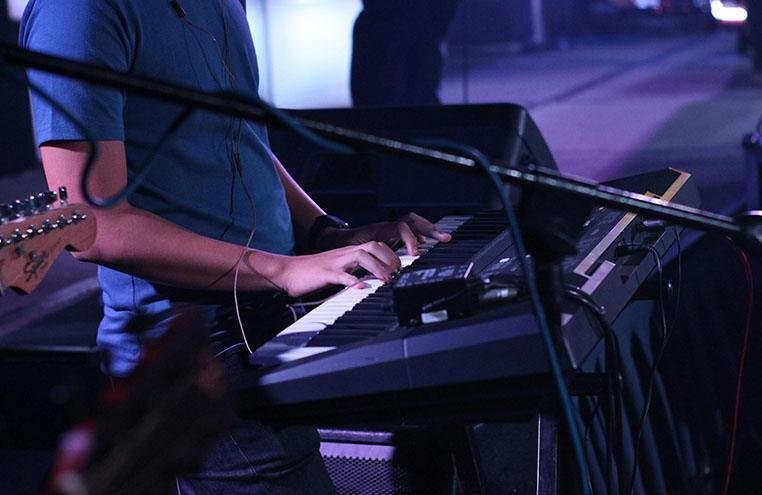 Musician playing a keyboard on stage under purple lighting