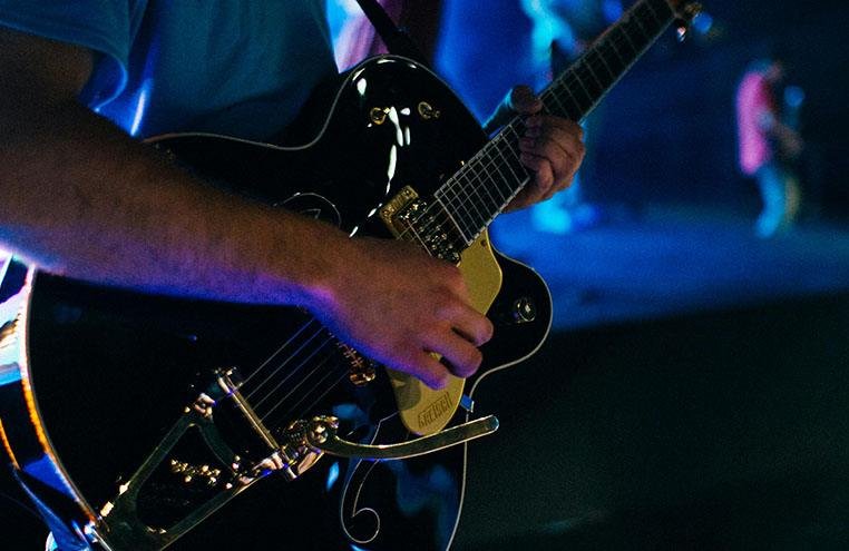 Close-up of a guitarist playing an electric guitar under blue lighting