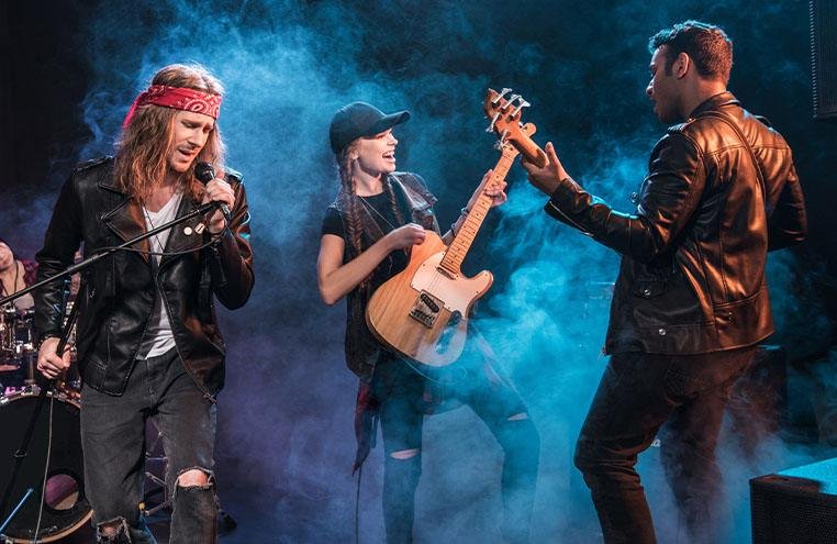 Band members celebrating on stage with guitars in hand and stage smoke behind
