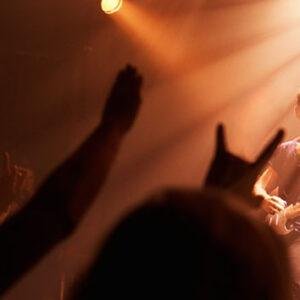 Crowd with raised hands enjoying a concert under warm stage lighting
