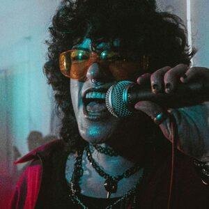 woman singing into a microphone under colourful retro lighting