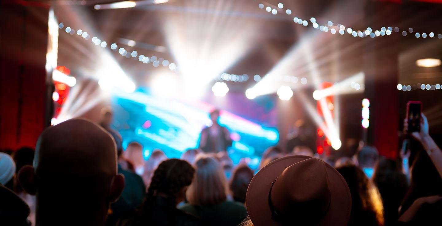 Concert crowd facing a brightly lit stage with dramatic lighting effects