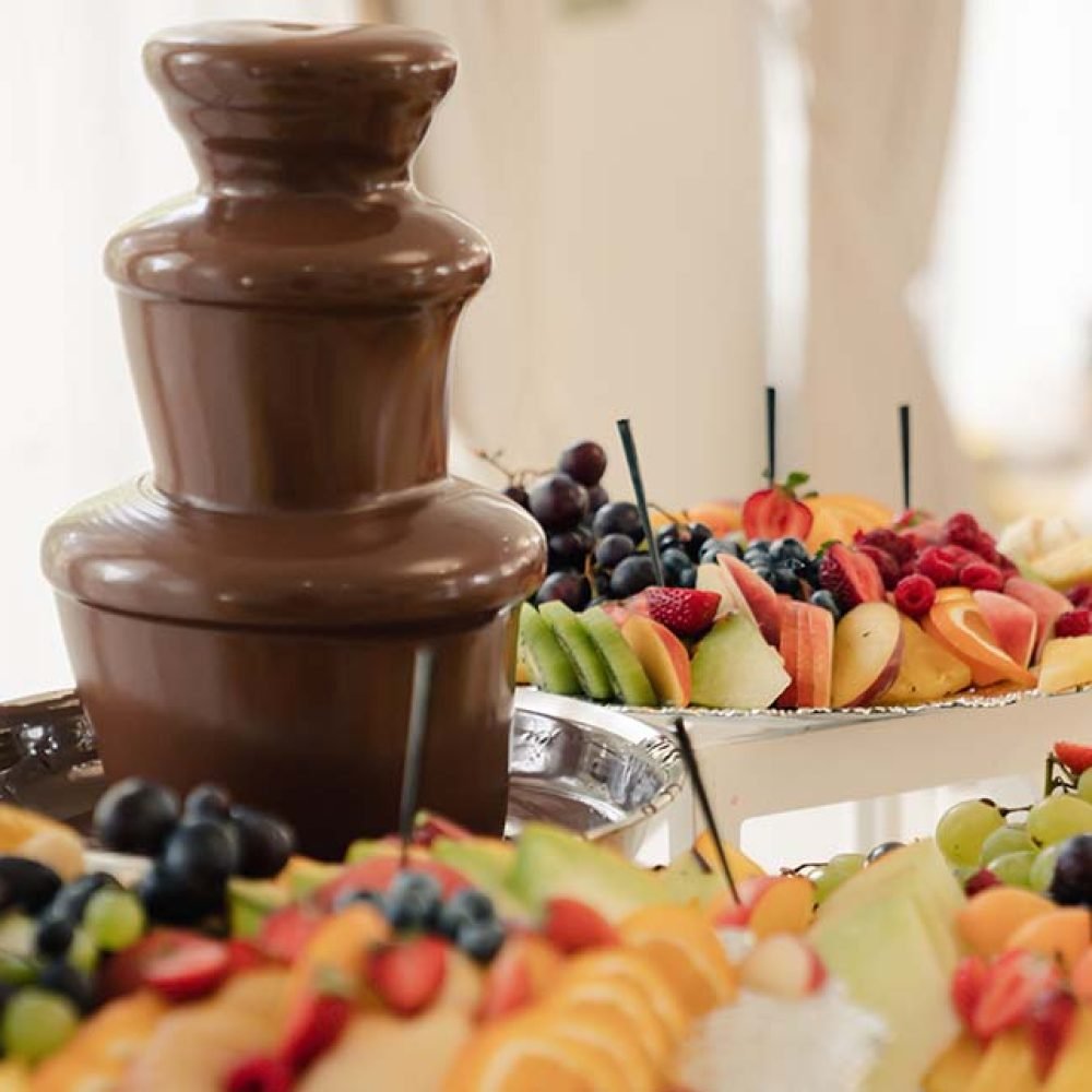 Chocolate fountain with skewered fruit displayed around the base.