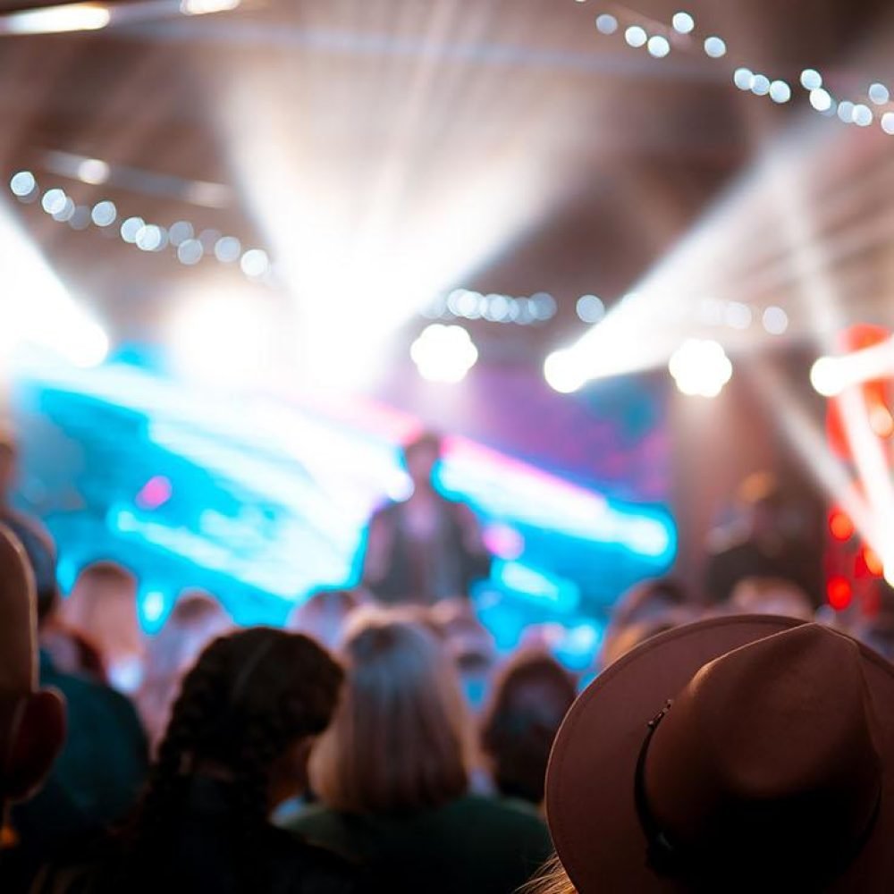 Concert crowd facing a brightly lit stage with dramatic lighting effects